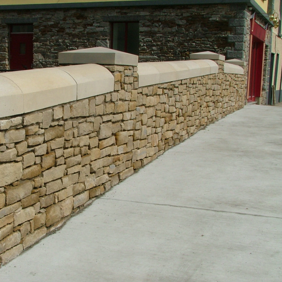 Stone wall with curved wall capping  next to a building entrance.