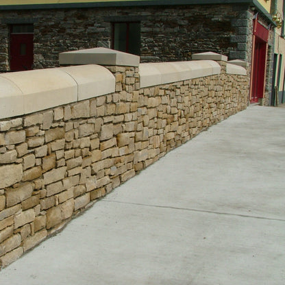 Stone wall with curved wall capping  next to a building entrance.