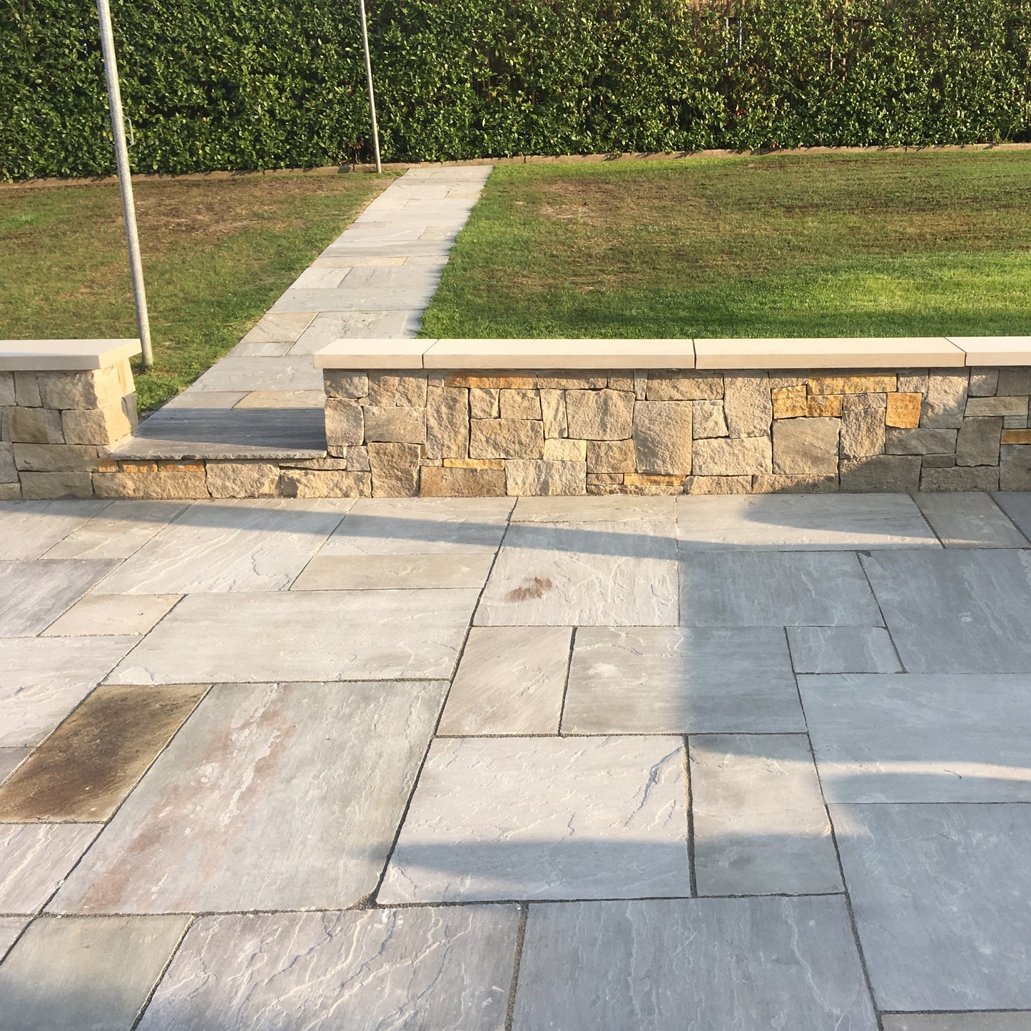 Low patio stone wall with flat sandstone wall capping leading to garden path.