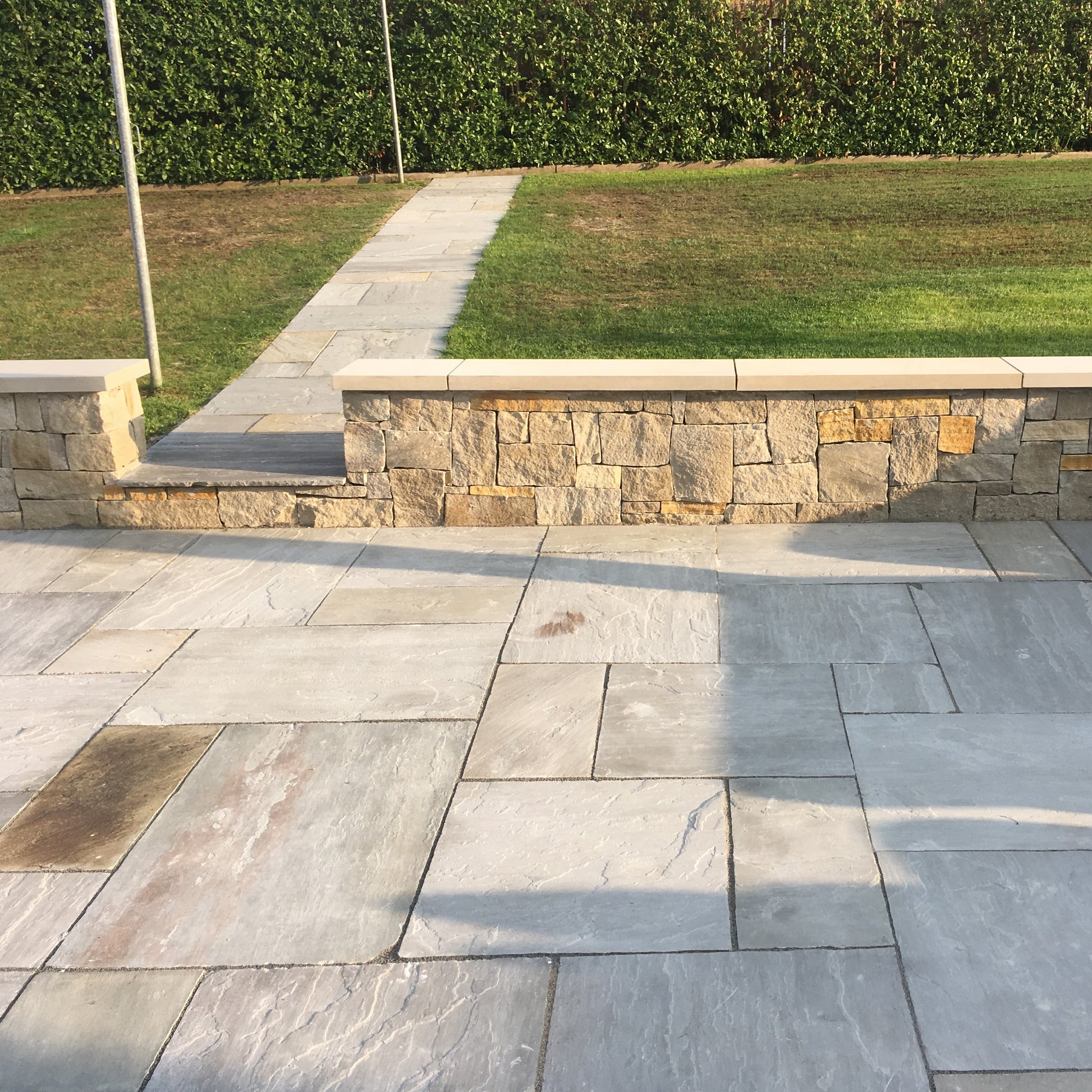Low patio stone wall with flat sandstone wall capping leading to garden path.