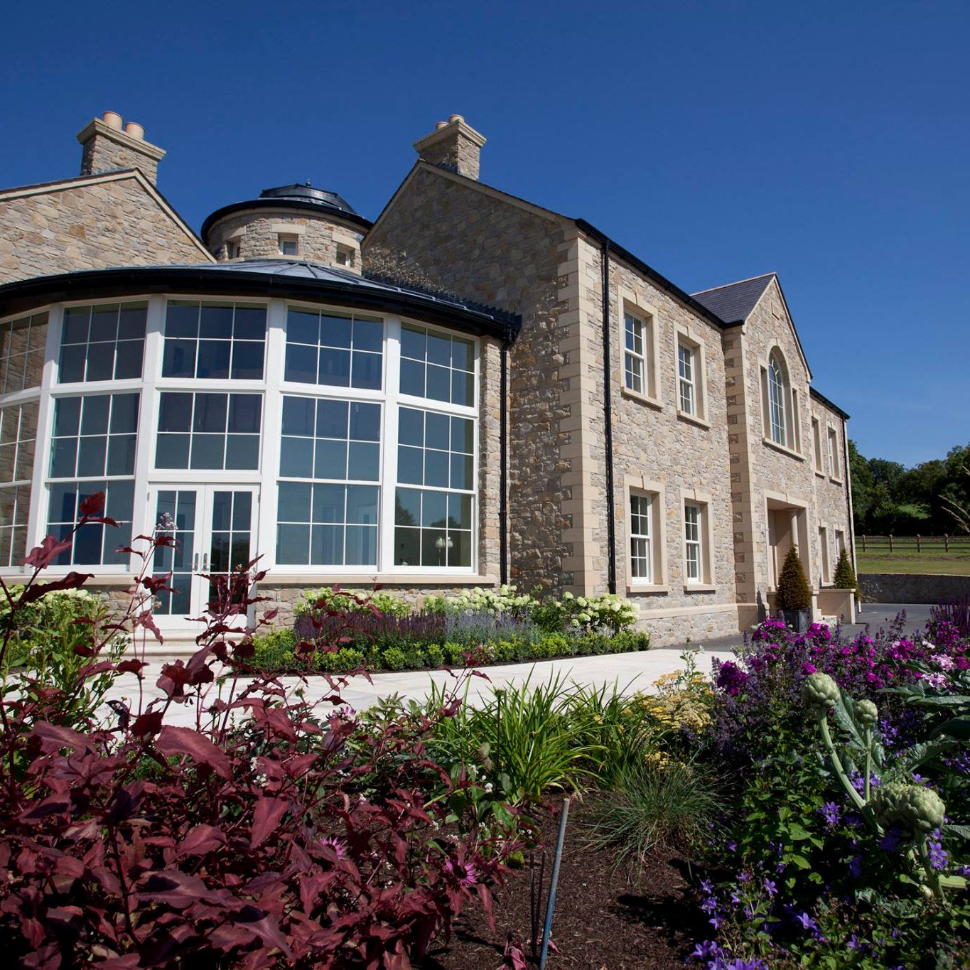 Large stone house with circular glass sunroom and bespoke sandstone window surrounds. 