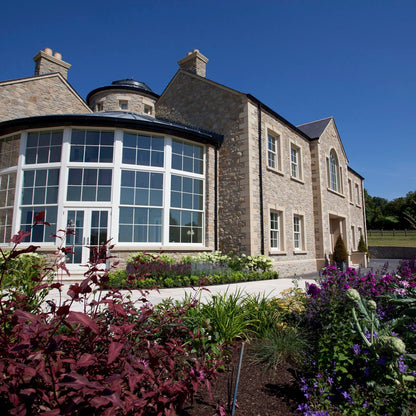 Large stone house with circular glass sunroom and bespoke sandstone window surrounds. 