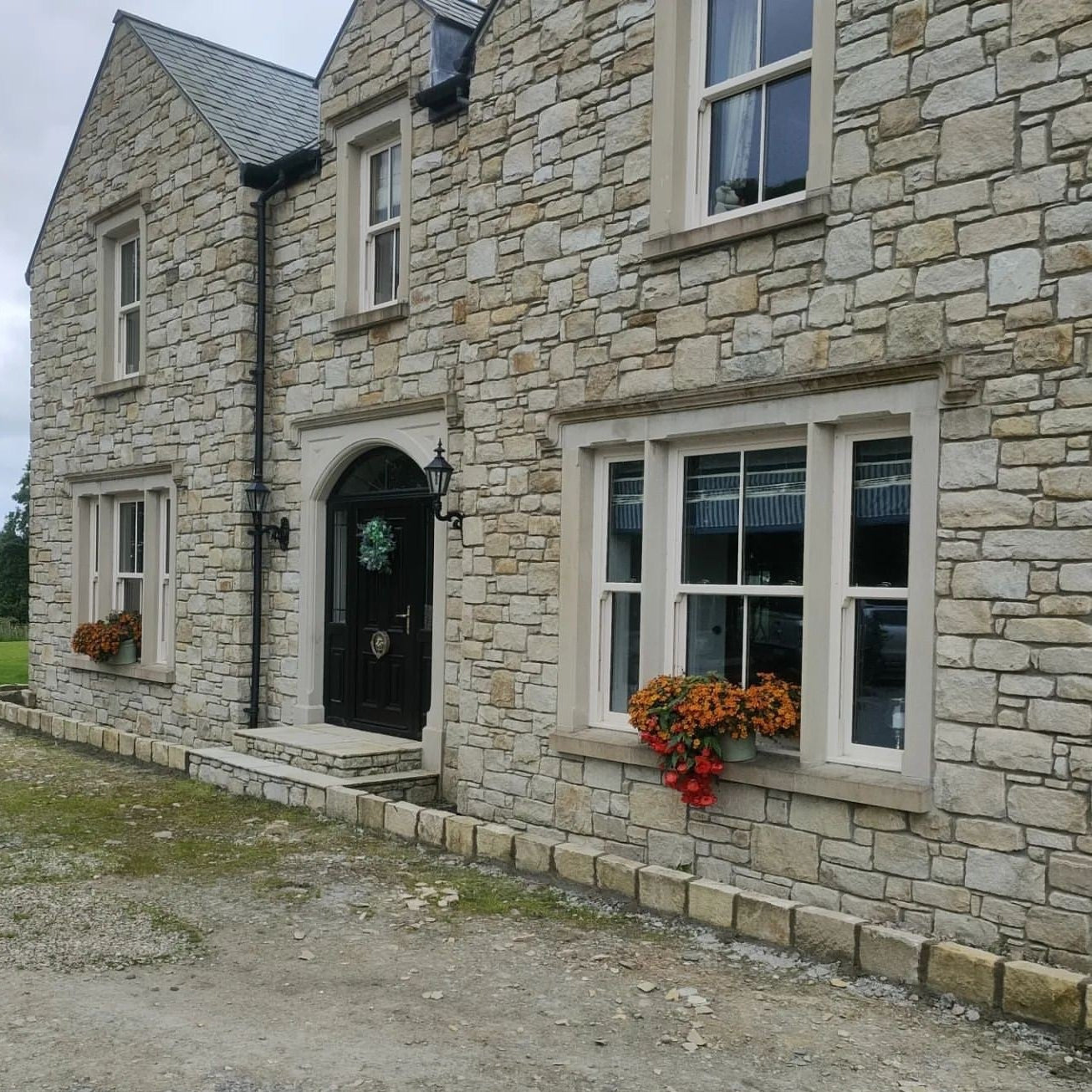 Stone house with bespoke Sandstone Window Surrounds and decorative flowers on a cloudy day. 