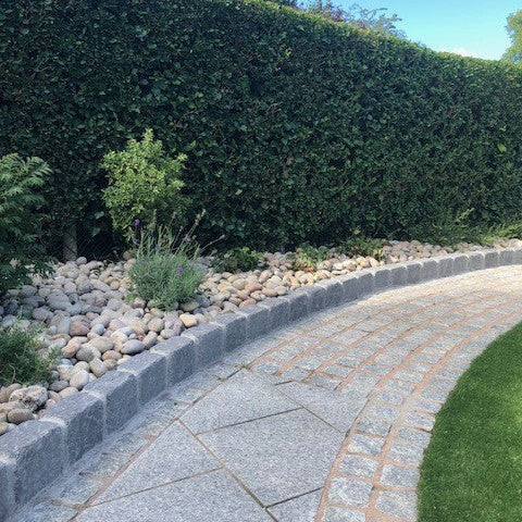 Pathway with planted rockery area in front of a large hedge. Rockery area features Scottish Beach Pebbles. 