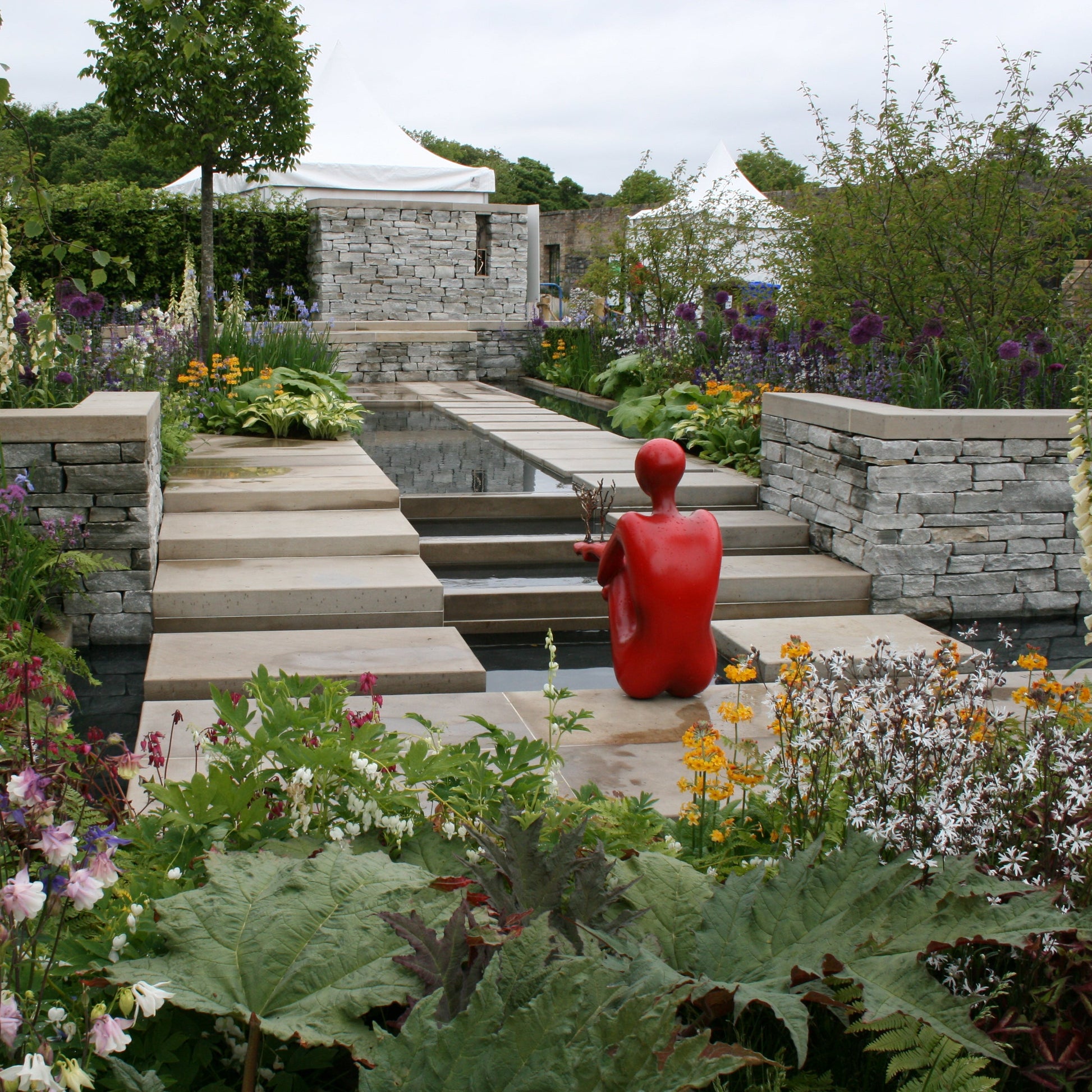 Garden scene with a red sculpture, stone steps, and flower beds. Garden wall completed in Silver Donegal Quartzite Garden Walling. 
