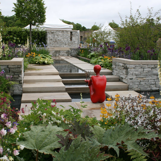 Garden scene with a red sculpture, stone steps, and flower beds. Garden wall completed in Silver Donegal Quartzite Garden Walling. 