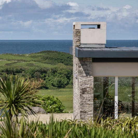 Close up of a contemporary house chimney completed in Silver Donegal Quartzite Garden Walling and Sea view in the background. 