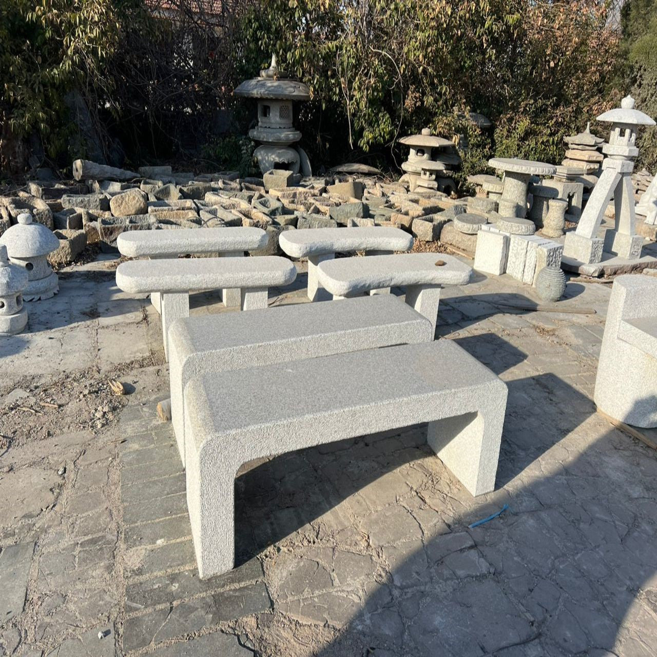 A polished silver granite bench with bush-hammered finishes on the surfaces, displayed in an outdoor setting with other stone features in the background.