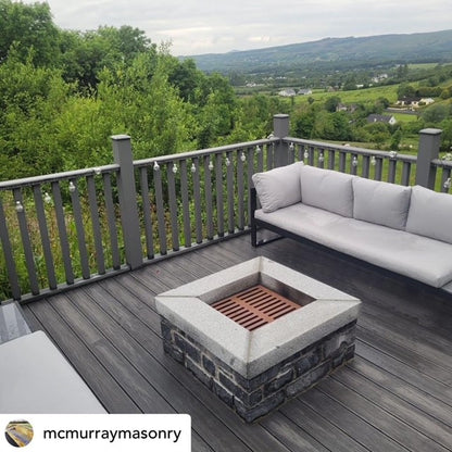Outdoor deck with grey sofa and stone fire pit, overlooking a scenic landscape. Fire pit completed with Silver Granite Wall Capping. 