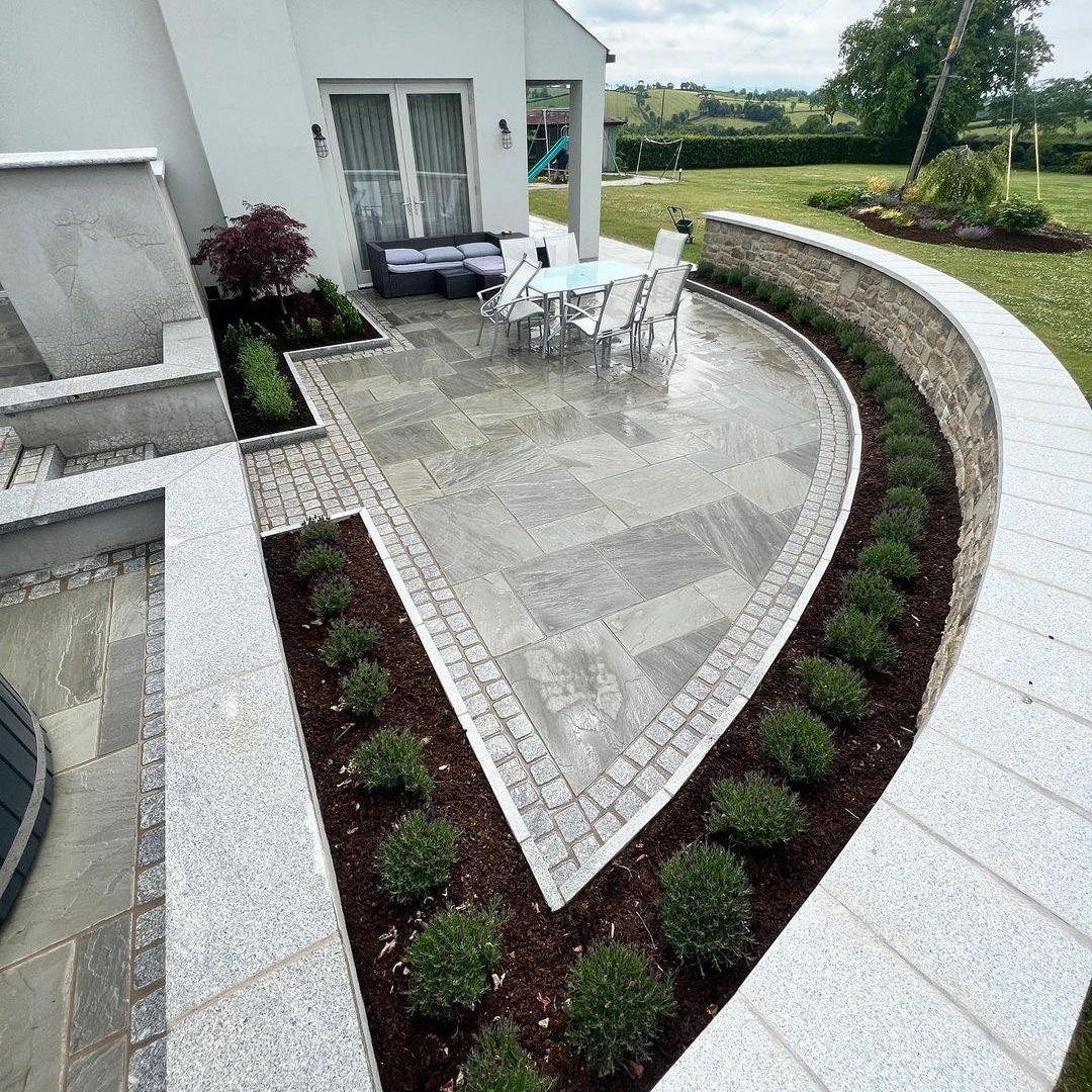 Modern patio area with outdoor furniture and landscaping in a residential setting. Patio wall completed using silver granite wall capping. 