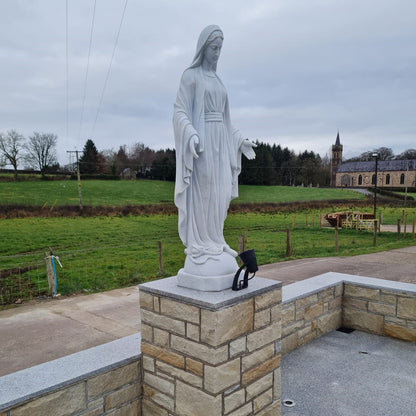 White statue of a religious figure on a stone pedestal with a church and fields in the background. Wall capped with Silver Granite. 
