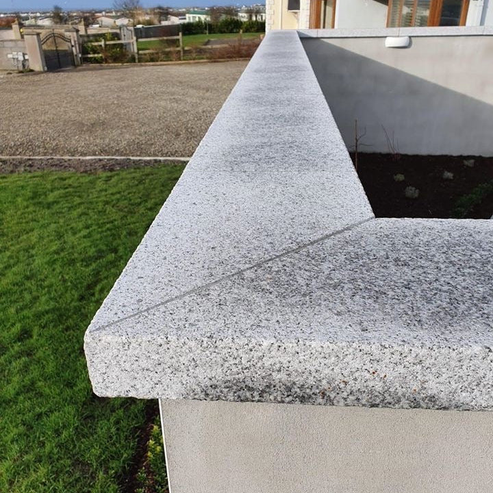 Patio wall with silver granite wall capping with driveway and house in the background. 