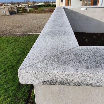 Patio wall with silver granite wall capping with driveway and house in the background. 