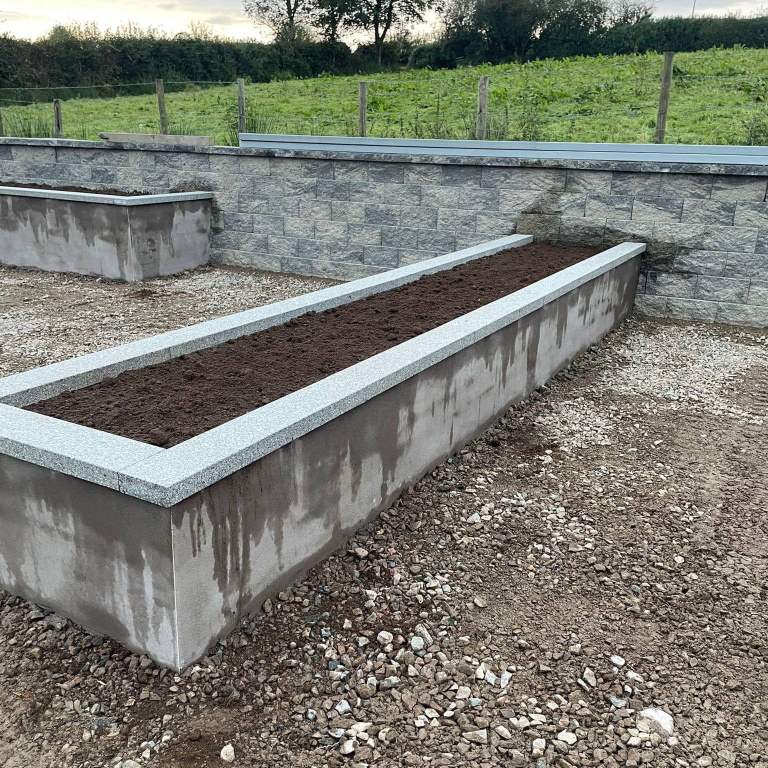 Long concrete planter with soil in an outdoor setting completed with Silver Granite Wall Capping. 