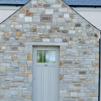 House exterior with stone façade and white door featuring bespoke silver granite door lintel. 
