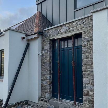 Under construction house with stone and white exterior, blue door with bespoke silver granite door lintel.
