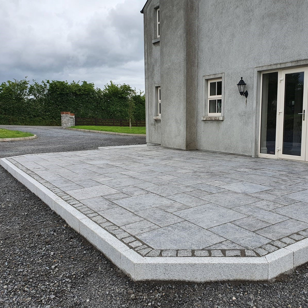 Patio area bordered by Blasted Silver Granite Kerbing. Driveway and trees in the background. 