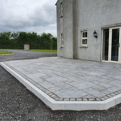 Patio area bordered by Blasted Silver Granite Kerbing. Driveway and trees in the background. 
