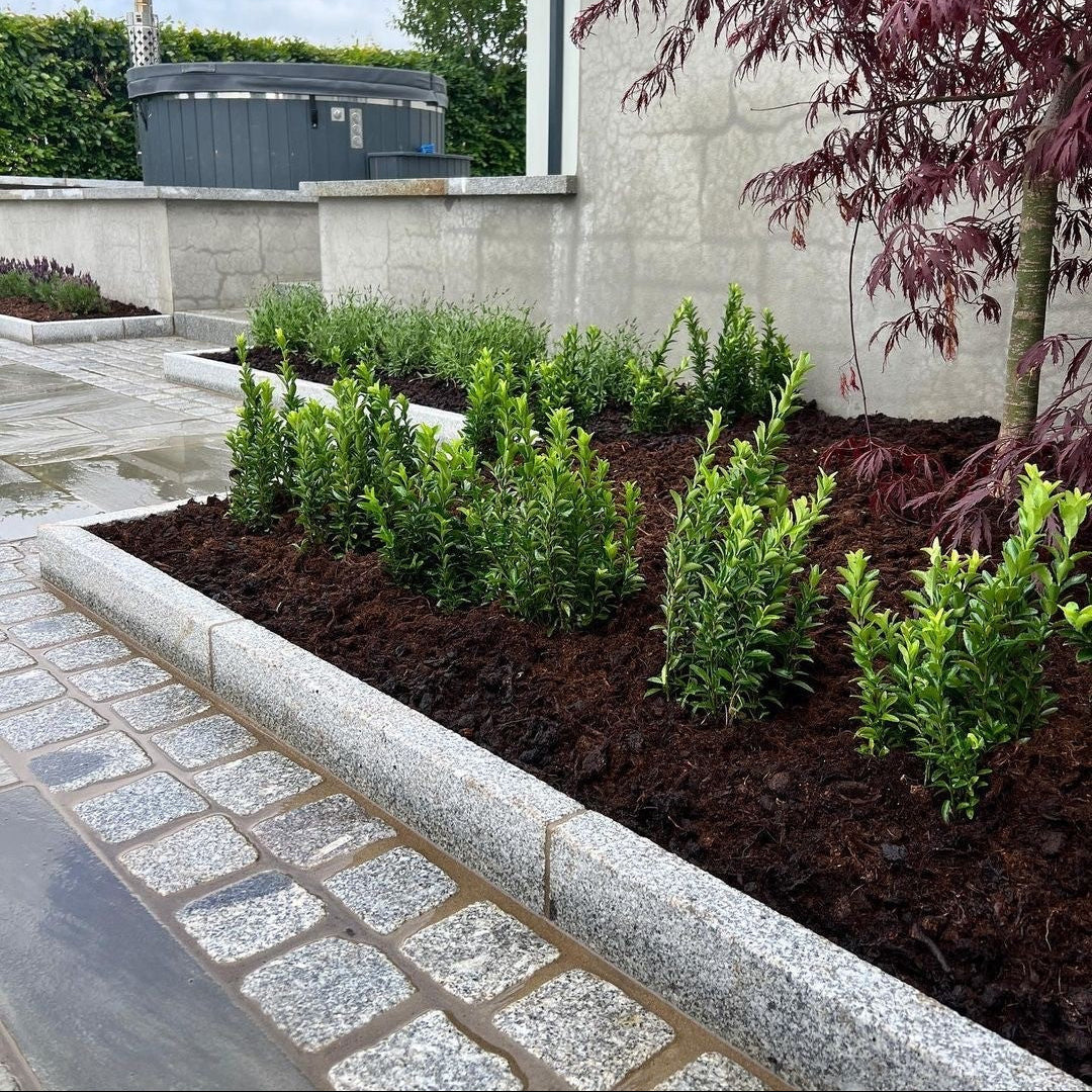 Planted beds lined by Silver Granite Kerbing and cobbles leading to a patio area with hot tub in the background. 