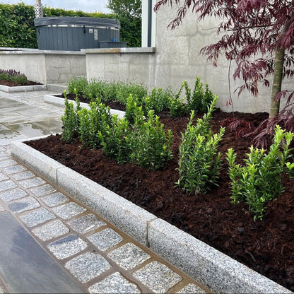 Planted beds lined by Silver Granite Kerbing and cobbles leading to a patio area with hot tub in the background. 