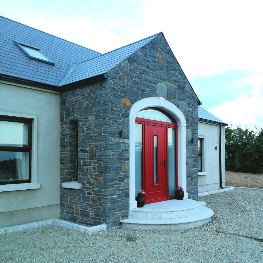 New build house with stone porch and red door. Planting beds created using Silver Granite Kerbs with pineapple finish. 