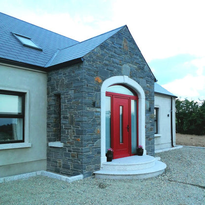 New build house with stone porch and red door. Planting beds created using Silver Granite Kerbs with pineapple finish. 