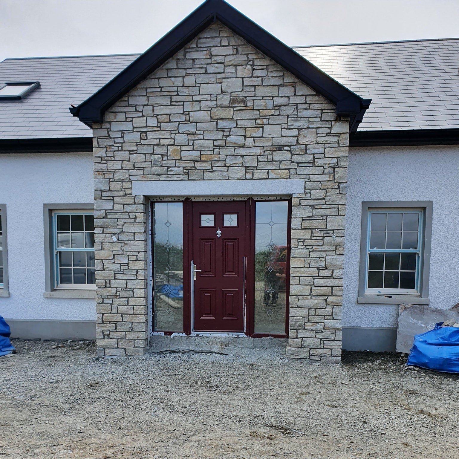 Stone façade of a building with a red door and silver granite door lintel. 