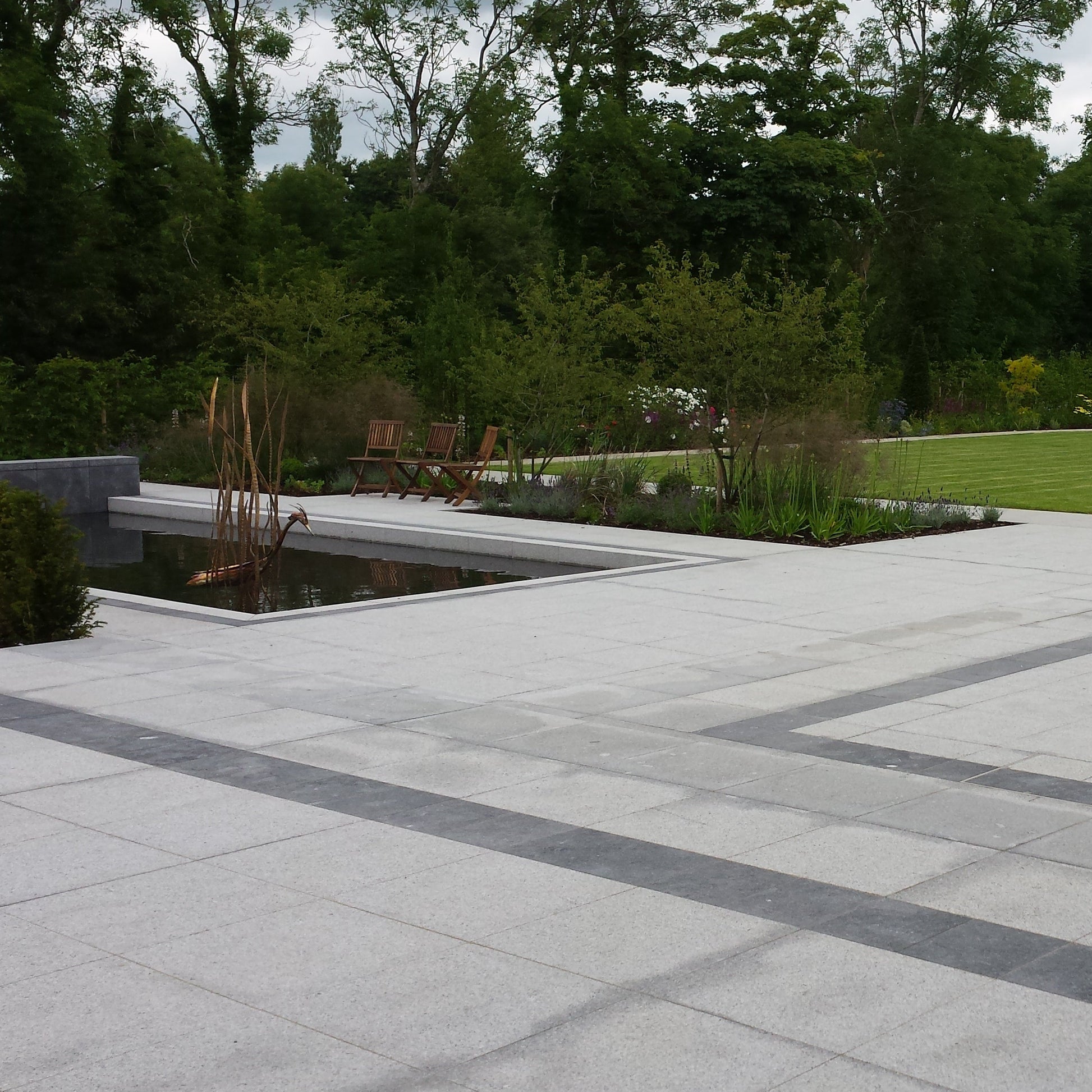 Large patio area in Silver Granite Paving in 600x600mm size. Patio features a pond and planting. 