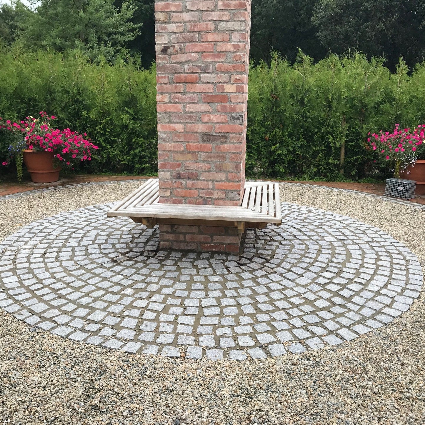 Silver Granite Paving Cobbles laid in circular design around a seating area with red bricks. Flowers and hedging in the background. 