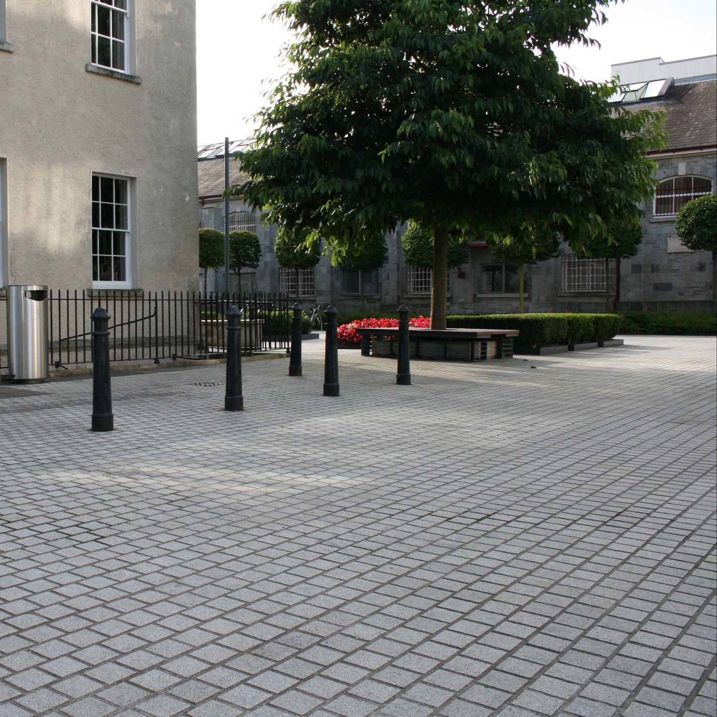 Paved area with a building and trees in the background. Paving completed using Sawn Silver Granite Paving Cobbles with a flamed finish. 