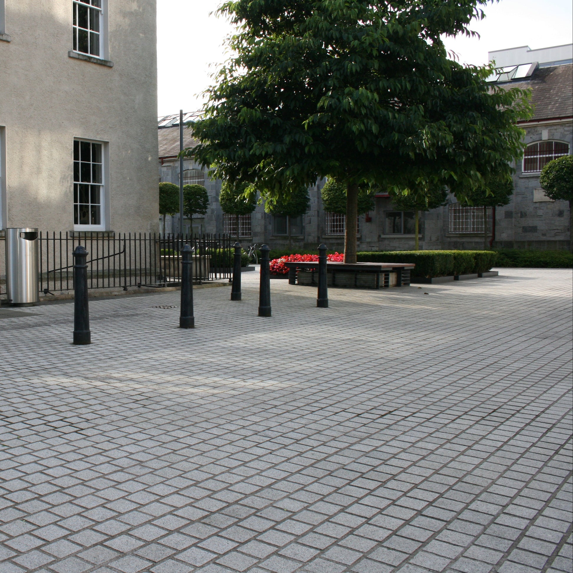 Paved area with a building and trees in the background. Paving completed using Sawn Silver Granite Paving Cobbles with a flamed finish. 