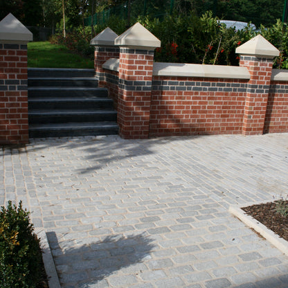 Brick wall with decorative caps and steps leading up to it, surrounded by greenery. Pathway is completed using Silver Granite Cobbles in 200 x 100mm size. 