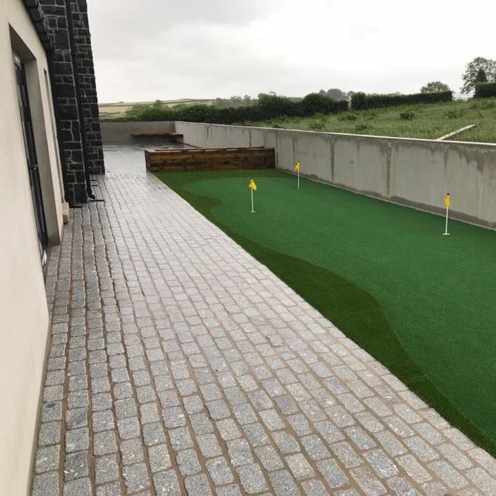 Outdoor area with a paved pathway using Silver Granite Cobbles leading to a golf putting area. 