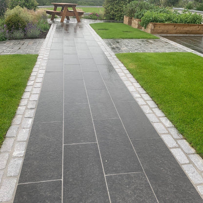 Paved pathway with grass on either side leading towards a picnic bench. Pathway edging completed using Silver Granite Cobbles in 200 x 100mm  