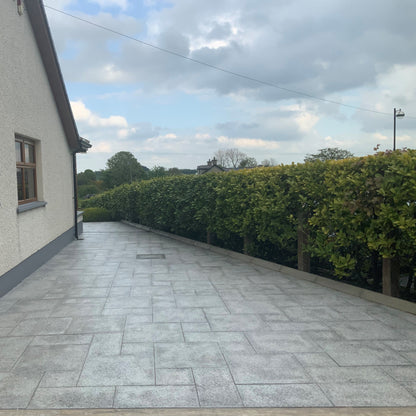 Patio area to the side of a house bordered by green hedging. Paving is Silver Granite in mixed patio pack sizes.  