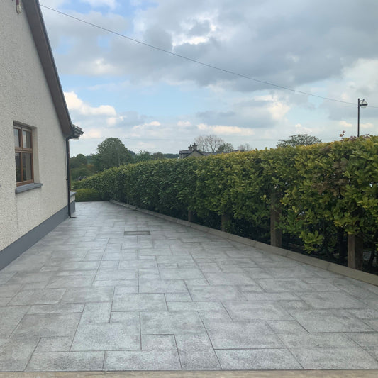 Patio area to the side of a house bordered by green hedging. Paving is Silver Granite in mixed patio pack sizes.  