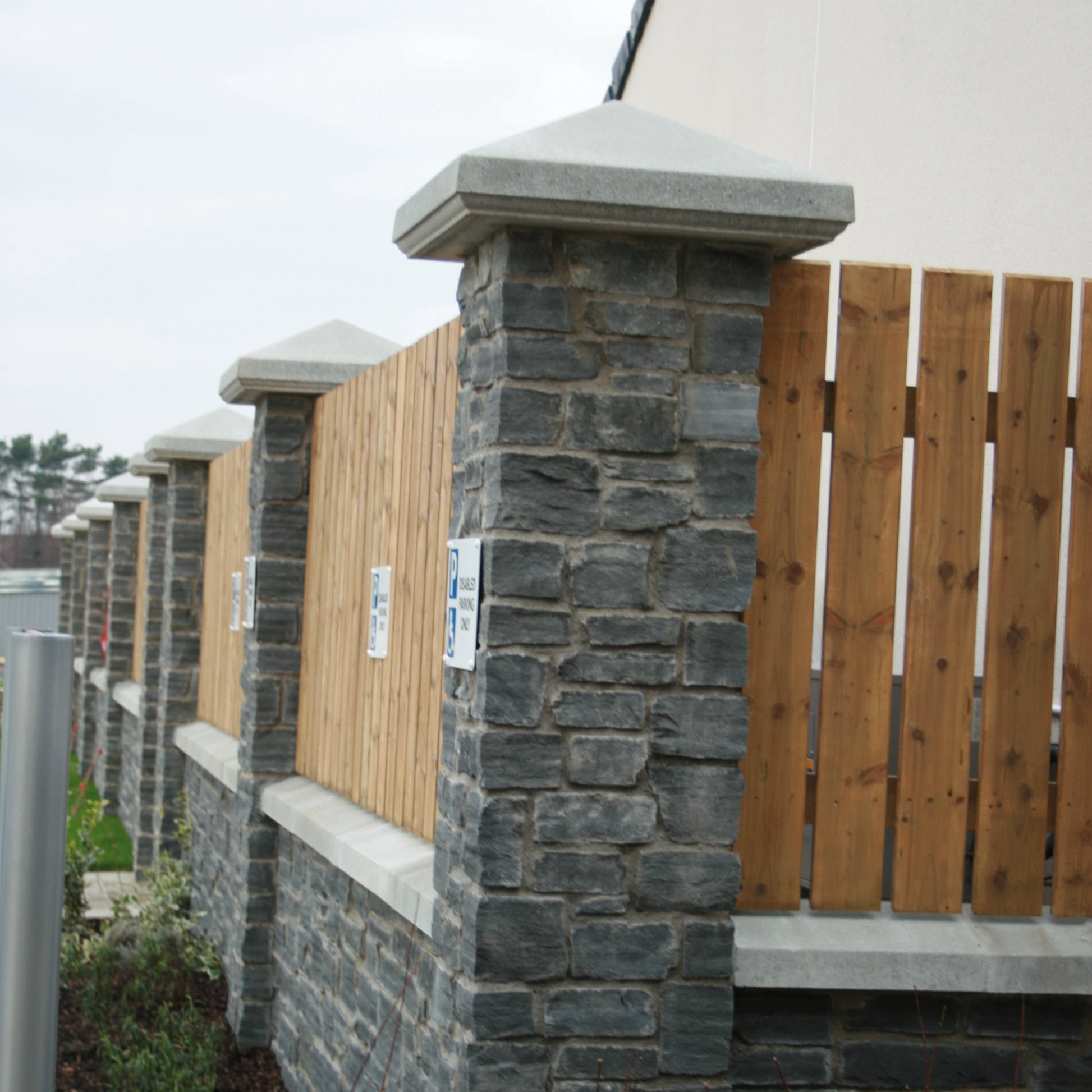 Large stone boundary wall with pillars and fencing in between. Pillars completed with bespoke silver granite pier caps.