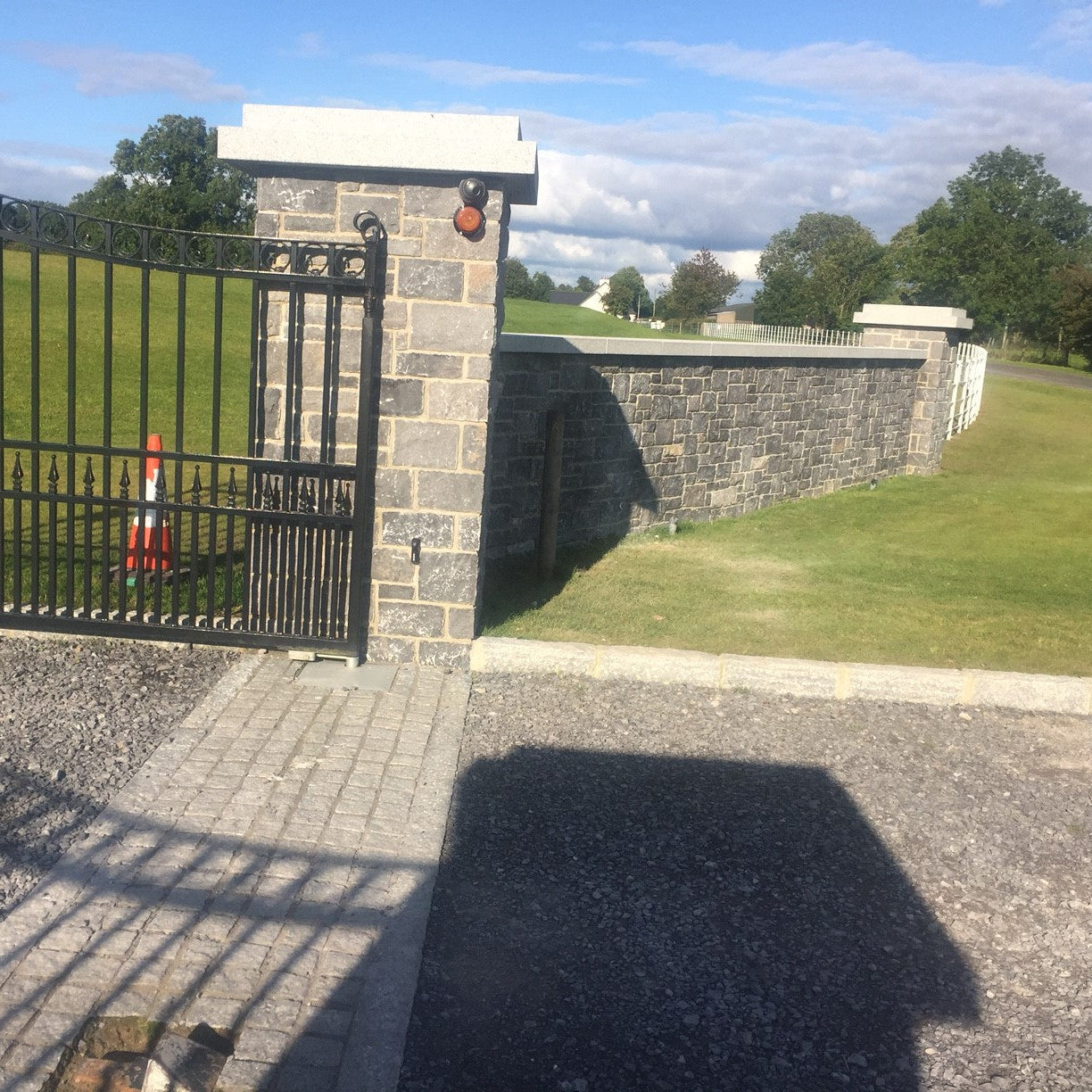 Stone wall with metal gate and grassy area. Wall completed with bespoke Silver Granite Pillar Caps and wall capping. 