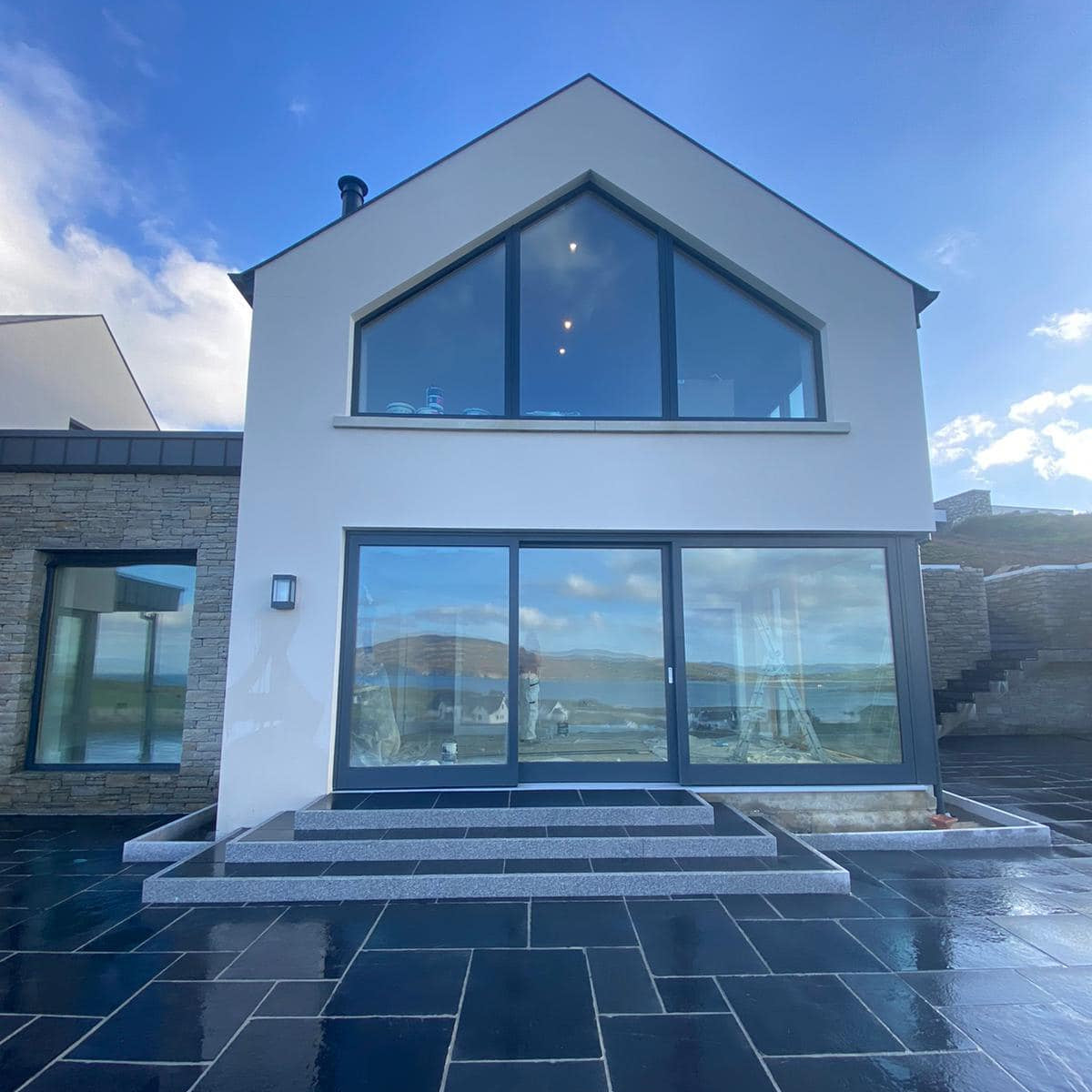 Modern house with large glass windows and a blue sky. Steps and planting beds completed using Silver Granite Pin Kerbs. 
