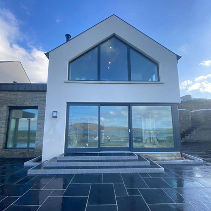 Modern house with large glass windows and a blue sky. Steps and planting beds completed using Silver Granite Pin Kerbs. 