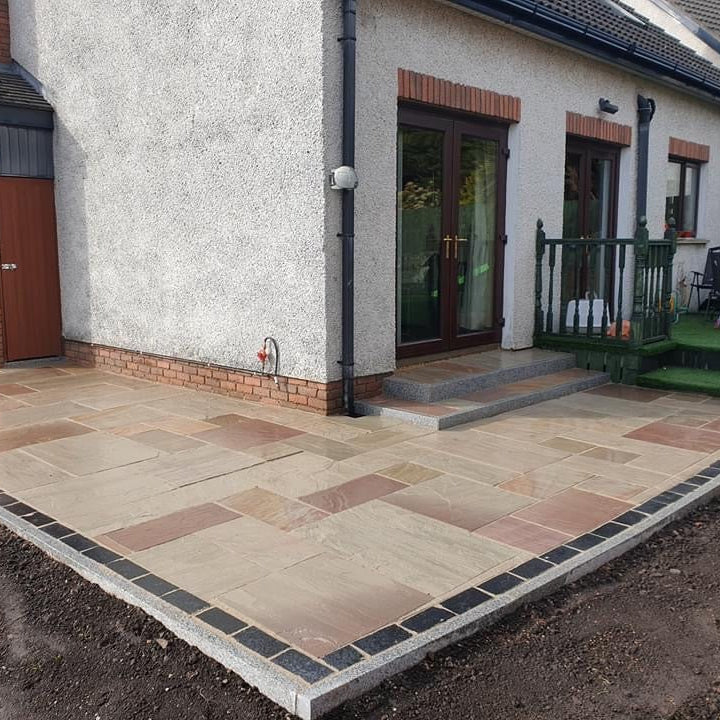 Paved patio area in front of a house with a brick wall and glass door. Patio and step edging completed using Silver Granite Pin Kerbing. 