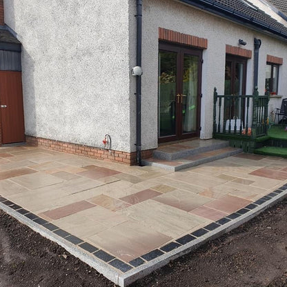 Paved patio area in front of a house with a brick wall and glass door. Patio and step edging completed using Silver Granite Pin Kerbing. 