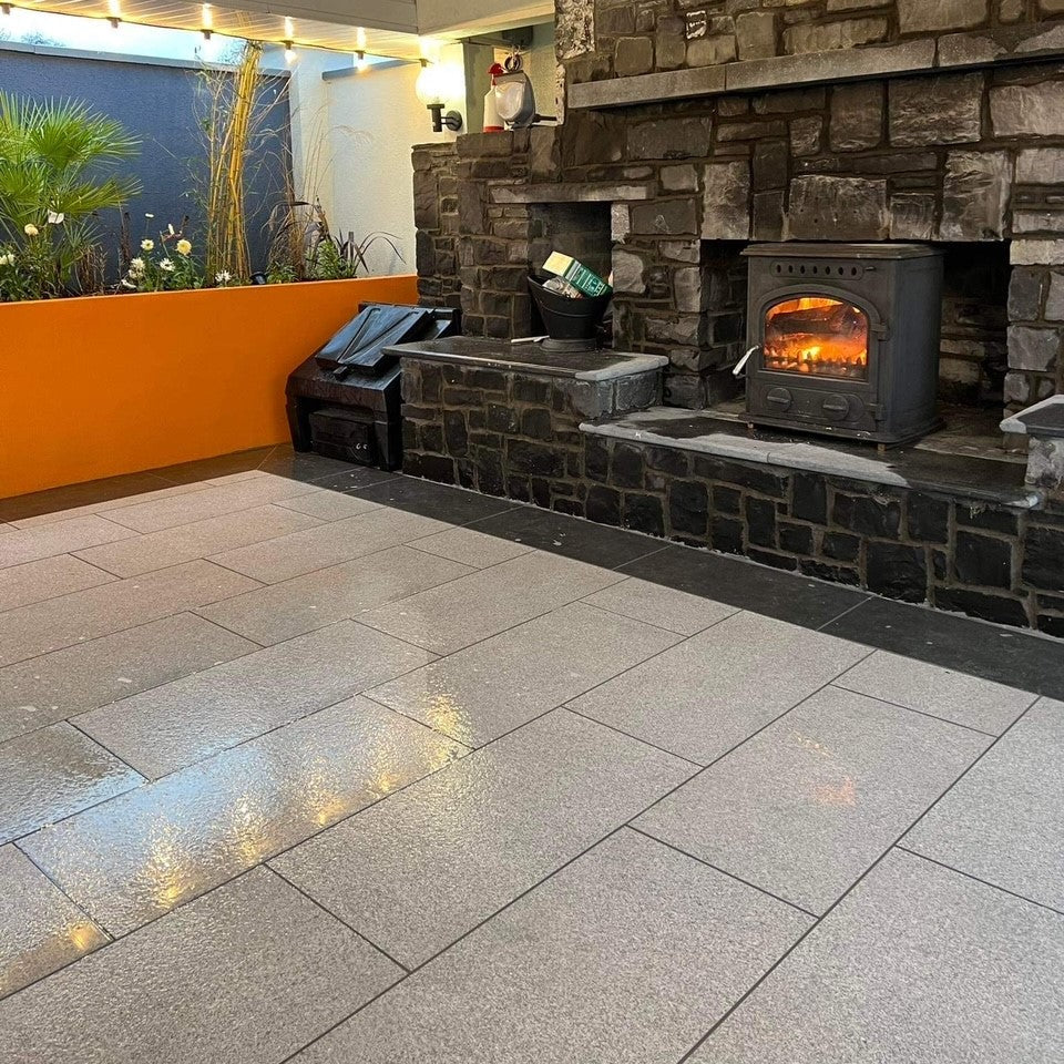 Outdoor patio with stone fireplace and tiled floor using Silver Granite Porcelain Tiles. 