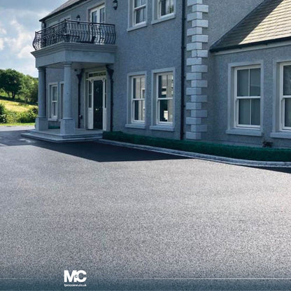 Driveway leading to a house with silver granite portico and a clear sky and greenery in the background.