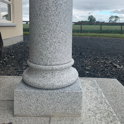 Granite column in front of a building with a cloudy sky and landscape in the background