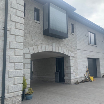 Modern house exterior with stone façade and garage doors. Featuring Bespoke Silver Granite Quoins.