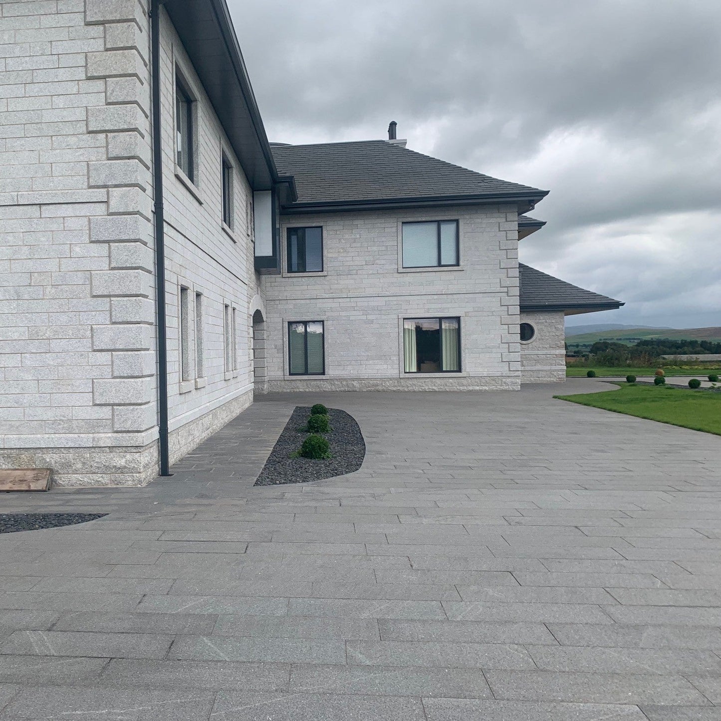 Modern house with a paved driveway and landscaped area under a cloudy sky. Featuring Bespoke Silver Granite Quoins