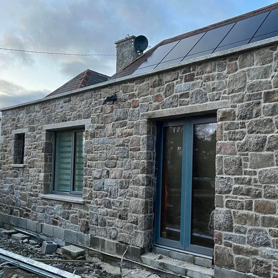 Stone masonry work on a building with solar panels and windows and door silver granite lintels and sills. 