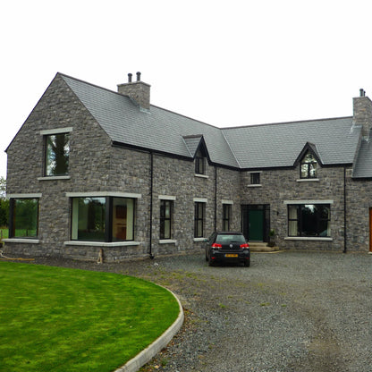Stone house with a driveway and car in front. Windows feature bespoke silver granite window Sills and  lintels. 