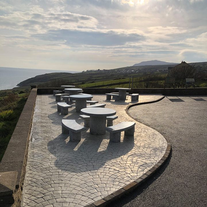 Outdoor seating area with Silver Granite round tables and benches on a stone patio overlooking a scenic landscape.
